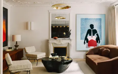 Un dormitorio eclectico con sofá marrón, dos sillones de tweed, mesa de centro de piedra negra, chimenea de mármol y arte abstracto vibrante.