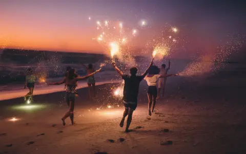 Giovani festeggiano il Ferragosto sulla Riviera Romagnola con scintille sulla spiaggia al tramonto.