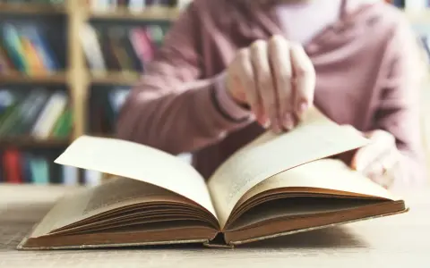 Otwarta księga na stole, w tle regały pełne książek. To początek podróży przez arcydzieła literatury światowej, lista skarbów do odkrycia.