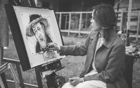 Artystka tworzy portret węglem. Jej ręka z pędzlem zbliża się do płótna, gdzie widoczna jest plama rysunek.
