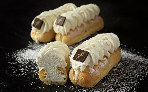 Trois éclairs chantilly généreusement garnis de crème fouettée, ornés d'un carré de chocolat, saupoudrés de sucre glace.