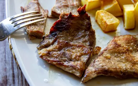 Jugosa blanqueta de cerdo a la plancha, servida con patatas fritas doradas. Un plato perfecto para disfrutar.