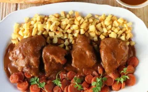 Delicioso jarrete de ternera estofado en salsa, acompañado de patatas fritas y zanahorias.