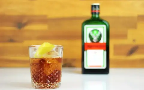 Jägermeister z pomarańczą to świetny drink. Na zdjęciu drink z lodem i plasterkiem pomarańczy obok butelki Jägermeister.
