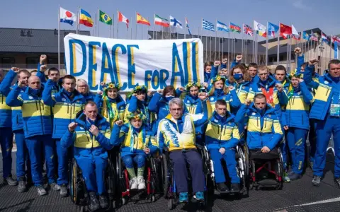 Ukraińska drużyna paraolimpijska z podniesionymi pięściami przed transparentem "Peace for All". Nadzieja na pokój na igrzyskach paraolimpijskich 2026.