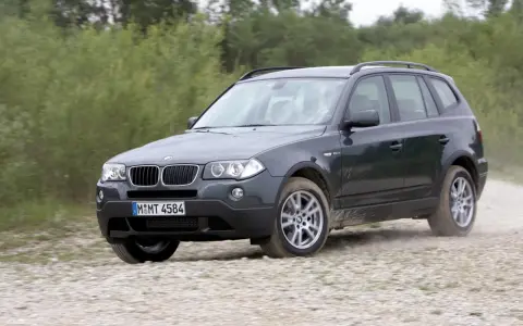 Ciemnoszary BMW X3 2024 na szutrowej drodze, otoczony zielenią.