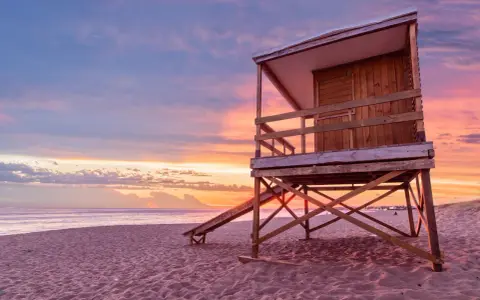 Drewniana wieża ratownicza na plaży o zachodzie słońca. Piasek i ocean tworzą tło dla tego malowniczego krajobrazu, który może być właśnie w Urugwaju, gdzie leży ten piękny kraj.