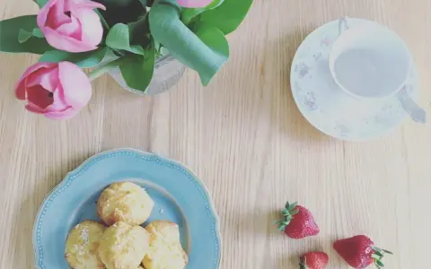 Chouquettes traditionnelles sur une assiette bleue, accompagnées de fraises et d'un bouquet de tulipes roses. Parfait pour une pause gourmande.