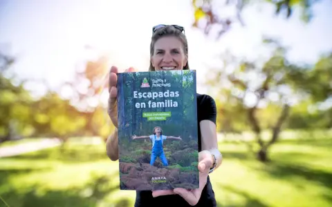 Mujer sonriente muestra libro "Escapadas en familia", con un niño en portada, ideal para viajes inolvidables para niños por España.