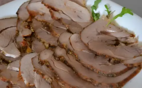 Pokrojony pieczony udziec z indyka z kością i skórą, przyprawiony ziołami, ułożony na białym talerzu.