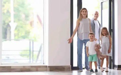 Familia de 4 miembros sonriendo y entrando a su nuevo hogar, pensando en el consumo medio electricidad.