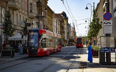 Czerwony tramwaj na ulicy w Katowicach. W tle kamienice i inny tramwaj. To widok na katowice stare miasto.