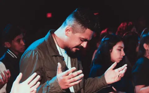 A man with his hands raised in prayer, part of a congregation following the order of prayer.