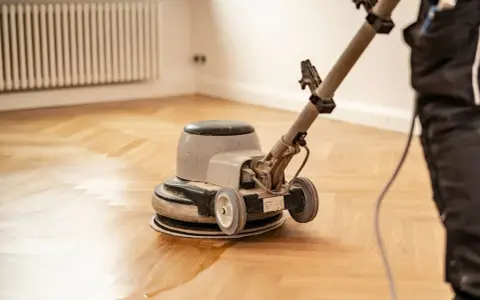 Polissage d'un parquet ancien avec une ponceuse. La rénovation redonne tout son éclat au bois.