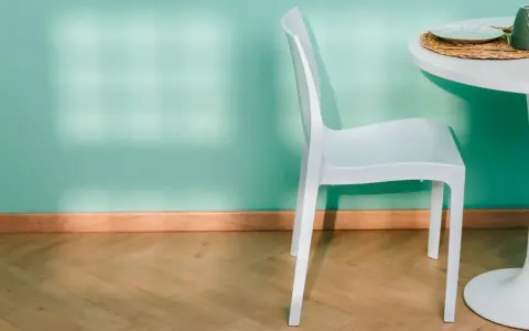 Un battiscopa in legno chiaro completa l'arredamento di una stanza con parete verde acqua, sedia bianca e tavolo.