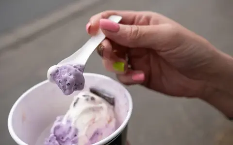 Eine Hand mit pink lackierten Nägeln hält einen Löffel mit zwei Kugeln Eis im Becher, italienisch.