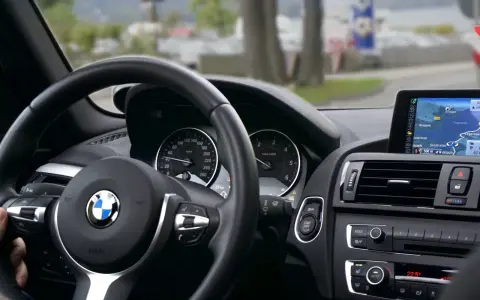 Wnętrze BMW z kierownicą i nawigacją. Kierowca sprawdza plan serwisowy przed podróżą.