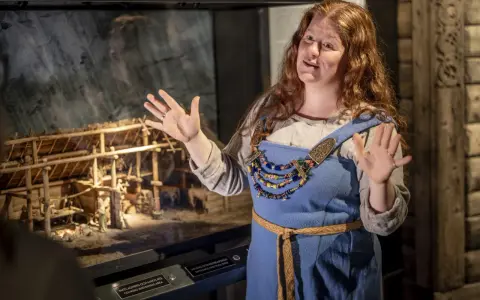 En guide i vikingakläder berättar vid en modell av en vikingaby på ett wikinger museum i Stockholm.