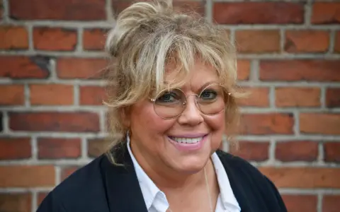 Marie Nilsson Lind ler mot kameran, med sitt blonda hår uppsatt och runda glasögon.