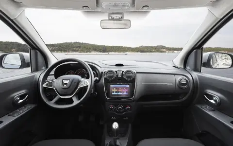 Interior del Dacia Lodgy con volante, pantalla táctil y palanca de cambios. El paisaje marino se ve a través del parabrisas.