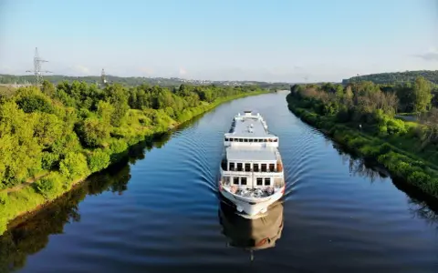 Nave da crociera solca un fiume sereno, con rive alberate che ricordano la bellezza naturale vicina alla capitale Russia.