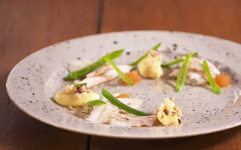 Vacker tallrik med piggvar recept: vit fisk, gröna bönor, orange rom och en krämig sås med nötter.