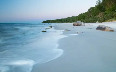Spokojne plaże nad Bałtykiem o świcie, z delikatnymi falami i kamieniami na piasku.