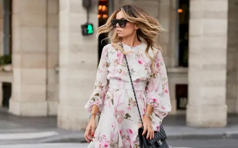 Frau mit luftgetrockneten, gesunden Haaren, die im Wind wehen, trägt ein Blumenkleid und Sonnenbrille.