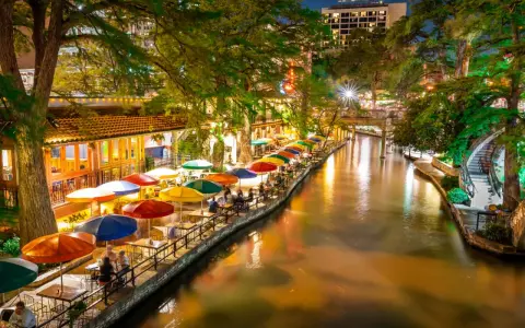 Bunte Sonnenschirme säumen den River Walk in San Antonio, wo Gäste abends in Restaurants am Wasser speisen.
