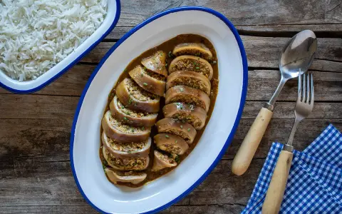 Calamares rellenos en salsa, servidos en una bandeja ovalada junto a un bol de arroz blanco. Cubiertos con cebollino picado.
