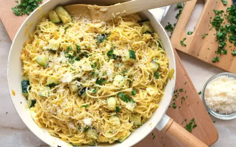 Pyszny makaron z jajkiem i cukinią, posypany parmezanem i świeżą natką pietruszki, gotowy do podania.