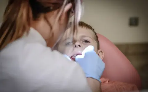 Chłopiec nie chce otworzyć ust u dentysty. Stomatolog próbuje go zbadać.