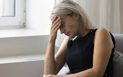 Kobieta z ręką na czole, cierpiąca na zawroty głowy związane z menopauzą.