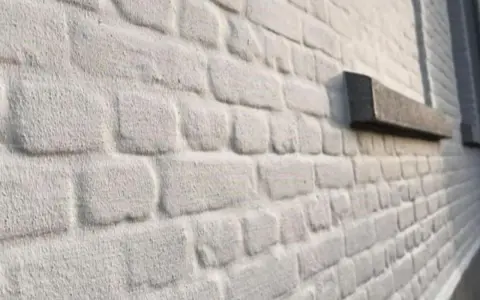 Mur en briques blanchies au badigeon à la chaux, avec un rebord de fenêtre en pierre sombre.