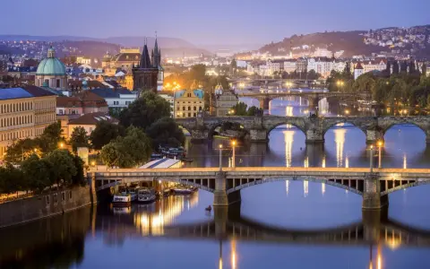 Praga nocą, z licznymi mostami na Wełtawie i oświetlonymi budynkami. Ciekawe ciekawostki o Czechach czekają na odkrycie w tym magicznym mieście.