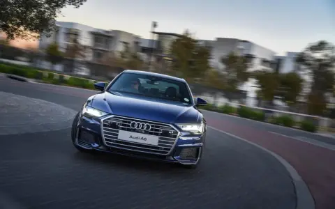 Niebieskie Audi A6 C8 w ruchu, z rozmazanym tłem budynków i drzew. Nawet przy potencjalnych usterkach, wygląda imponująco.