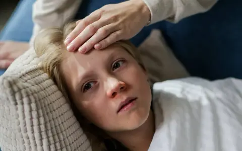 Niña con fiebre, su frente tocada por una mano. Posiblemente un caso de mononucleosis en niños.
