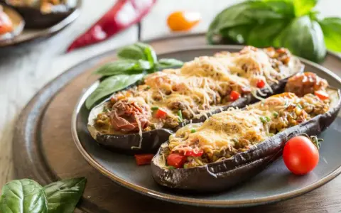 Berenjenas rellenas de atún, gratinadas con queso y decoradas con albahaca y tomate. Un plato delicioso y fácil de preparar.