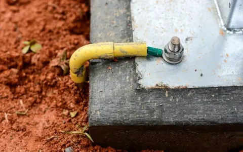 Connexion de la prise de terre maison à une structure métallique, assurant la sécurité électrique. Le câble jaune est relié à une cosse verte, fixée par un boulon.