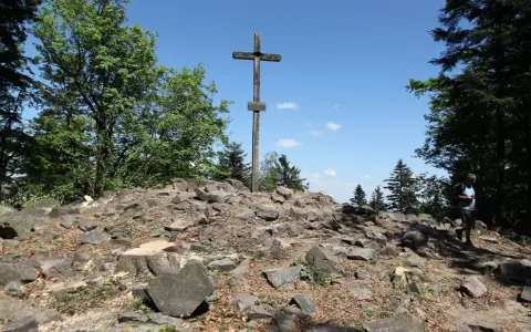 Kamienisty szczyt z drewnianym krzyżem, otoczony drzewami. Idealne miejsce na wędrówkę po górach świętokrzyskich szlaki.