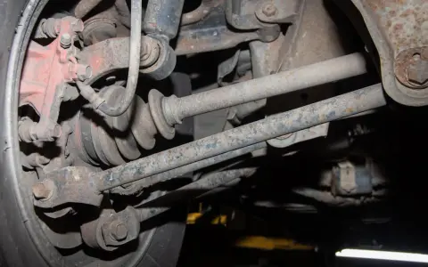 Widok od spodu na skorodowany wielowahacz z widoczną piastą, przegubem i elementami zawieszenia.