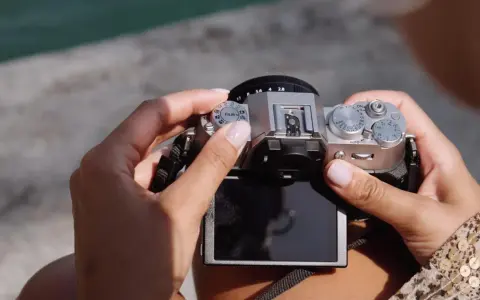 Dłonie trzymają srebrny aparat Fujifilm XT50, obracając pokrętło trybów filmowych.