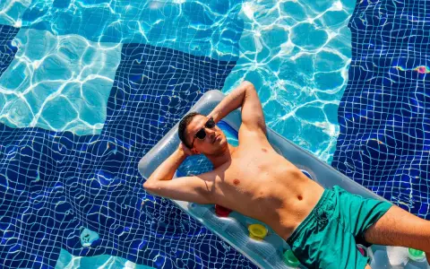 Uomo rilassato su un materassino in piscina, con gli occhiali da sole. Chissà se posso andare al mare se prendo l'antibiotico, pensa.