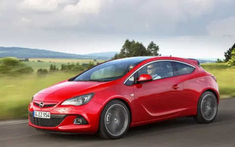 Czerwony Opel Astra J 1.4 Turbo z parą na pokładzie przemierza malowniczą trasę wśród zielonych pól i wzgórz.