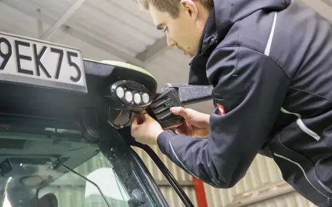 Mężczyzna montuje lampy LED na ciągniku. Dowiedz się, jak podłączyć lampy LED w ciągniku, aby poprawić widoczność w nocy.
