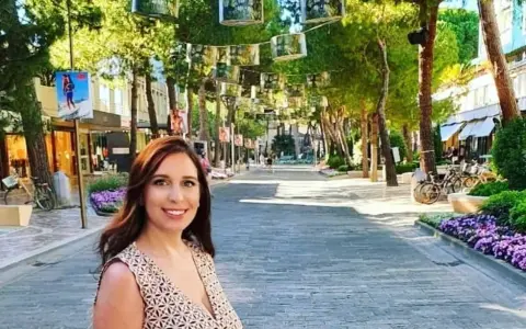 Donna sorridente in una strada alberata con negozi e fiori viola, un'atmosfera estiva nel centro di Milano Marittima.