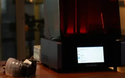 A HeyGears resin printer with a red interior light. Beside it, a camera lens. This setup hints at the process of how long to cure resin prints.
