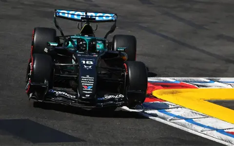 El coche de F1 Aston Martin número 18 se inclina en una curva, con sus neumáticos rozando la línea de la pista.