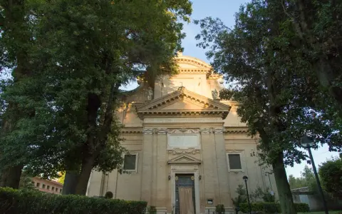 A serene church facade at Tre Fontane, Rome, bathed in golden light, framed by lush green trees.