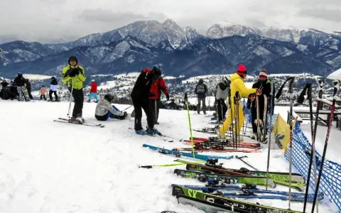 Ludzie na nartach i snowboardach na stoku, w tle góry. Zastanawiasz się, ile się idzie na Gubałówkę? Tu jest zimowo i aktywnie!